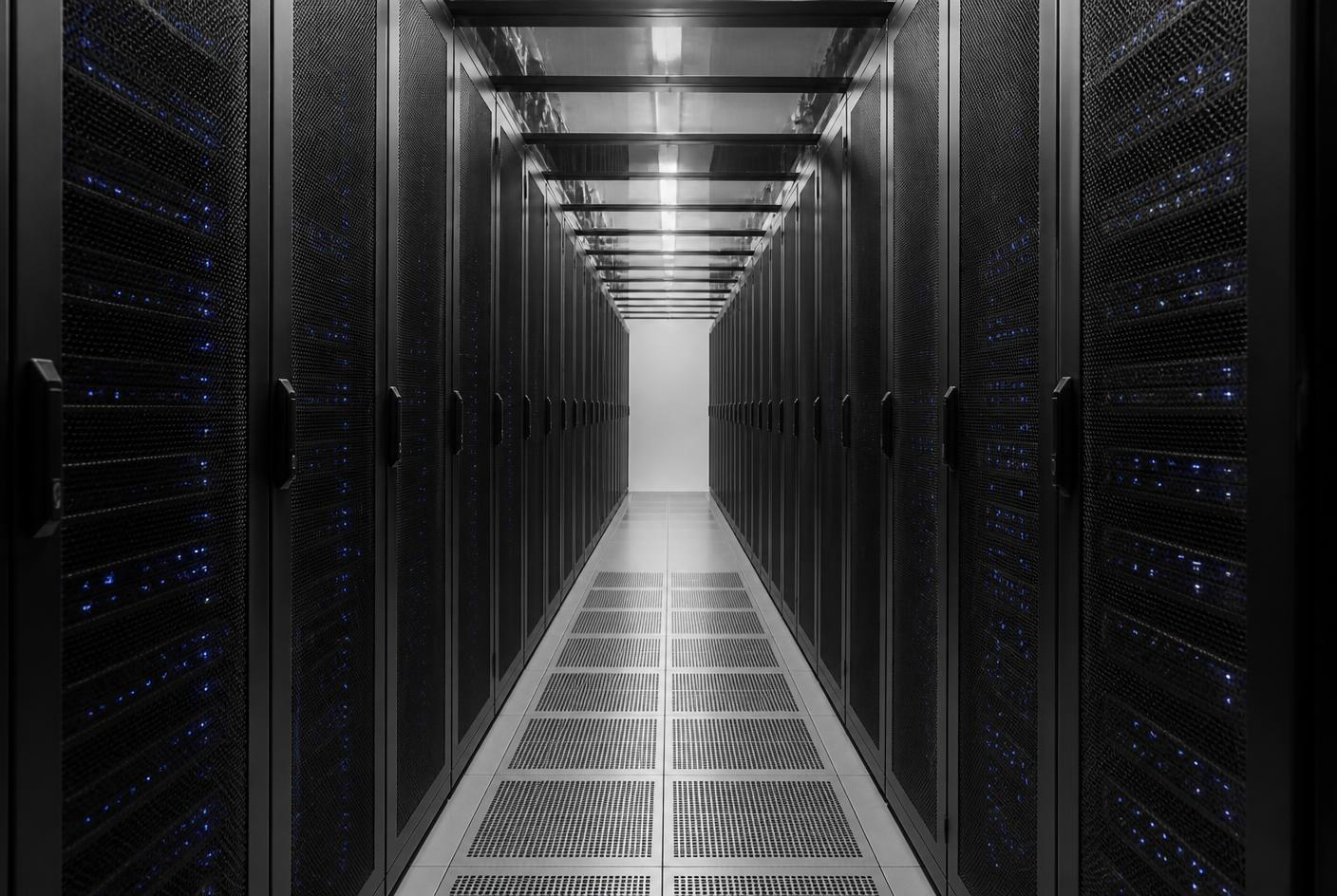 Corridor of server cabinets in a data centre, lit by overhead strip lighting